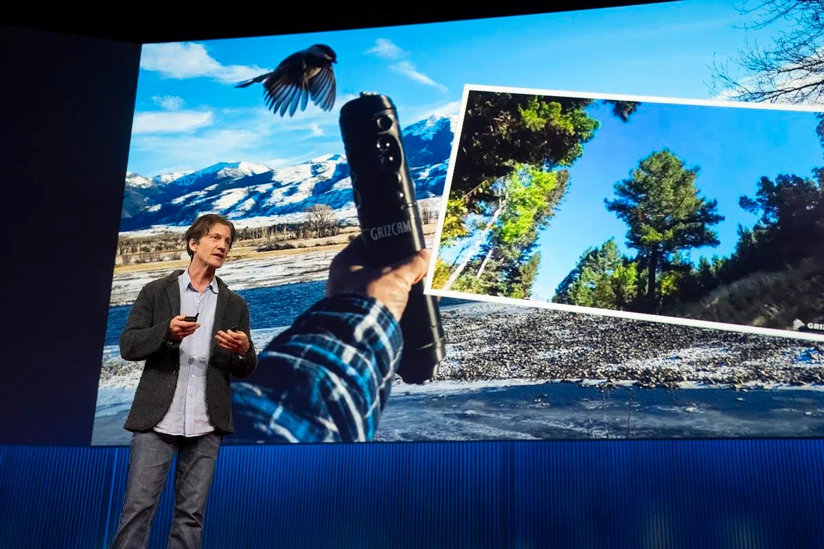 Jeff Reed on stage presenting a GrizCam device against a slide of mountain scenery